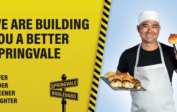 Baker holding bun with the text 'we are building you a better Springvale'