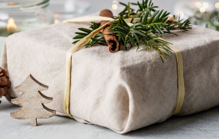 a gift wrapped in fabric and decorated with foliage and a pinecone