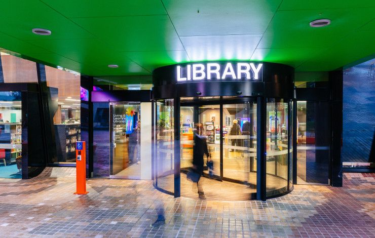 Revolving door below a green ceiling and a lit-up sign that says Library