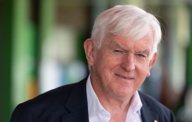 Man with white hair, dressed in a white shirt and black jacket, smiling at the camera