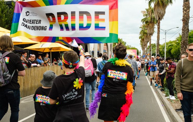 A group of people walking down a street lined by crowds under a banner that reads Greater Dandenong Pride