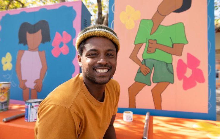 Man wearing a beanie and smiling at the camera in front of brightly painted art panels.