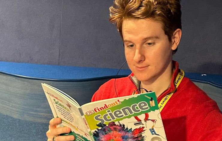 Young library staff member reading a book in the library.