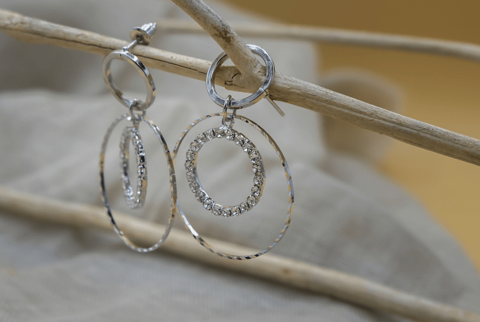 Two circular silver earrings hanging on a stick.