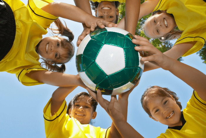 Young soccer players holding a soccer ball and looking down at the camera.