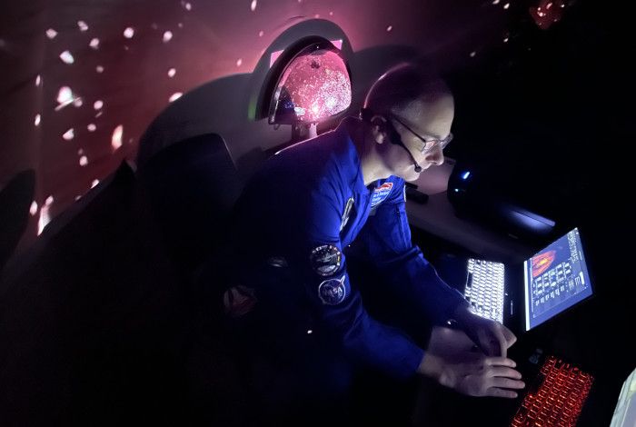 Person dressed as astronaut using a laptop in a planetarium.