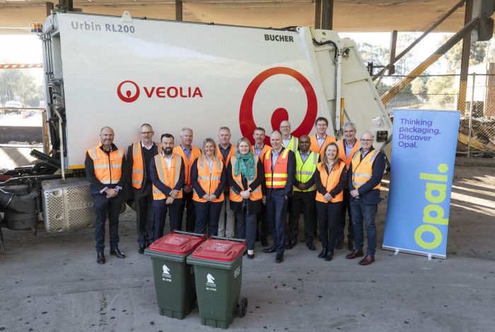 A group of people in high vis vests stood in front of a garbage truck.