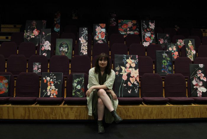 Artist Josephine Mead sitting on theatre seats with their paintings.