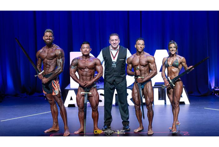 Male and female bodybuilders lined up on stage, holding swords