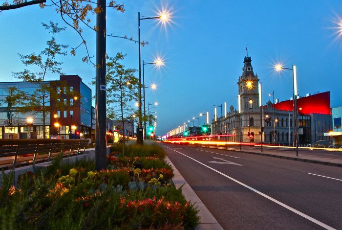 Looking down astreet at twilight with an historic clock tower and office buildings in the background