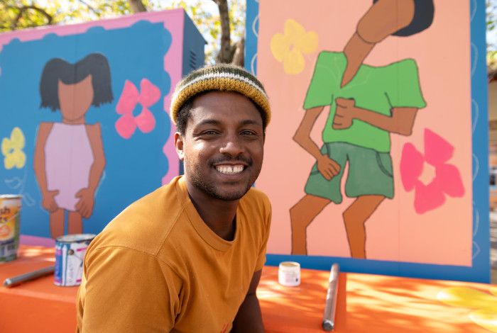 Man wearing a beanie and smiling at the camera in front of brightly painted art panels.