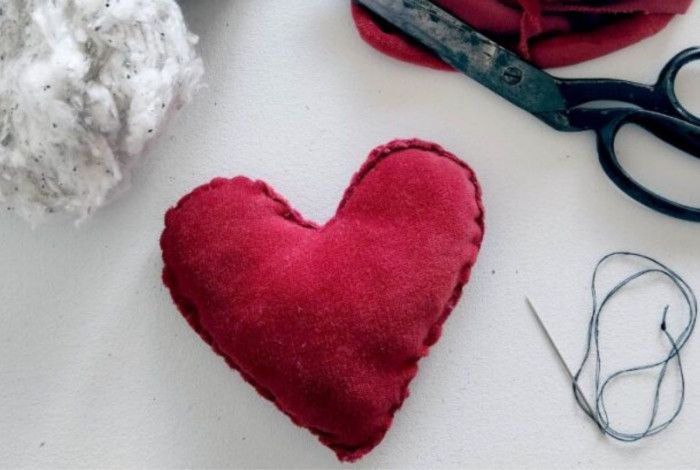 A red fabric heart surrounded by scissors, a needle and thread.