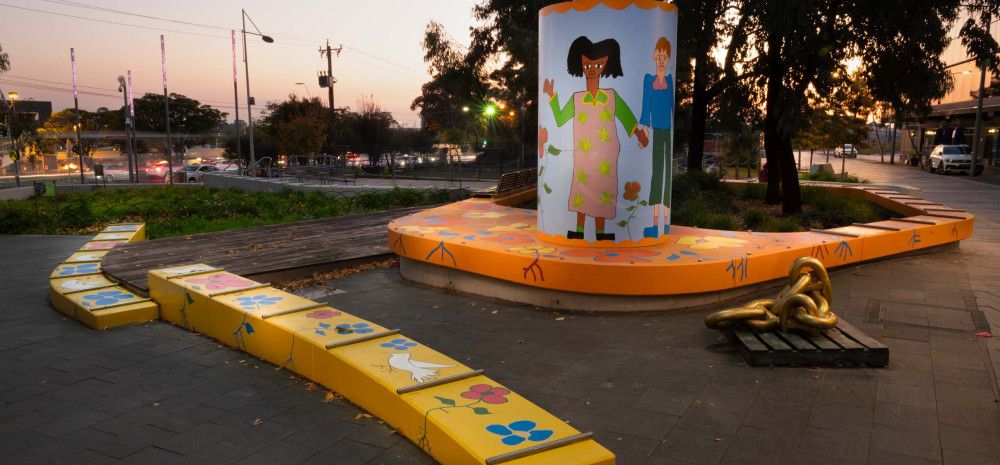 Seating and a light box in a public space decorated with colourful paintings of people