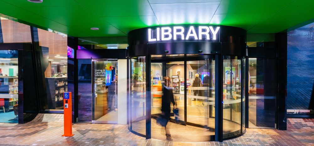 Revolving door below a green ceiling and a lit-up sign that says Library