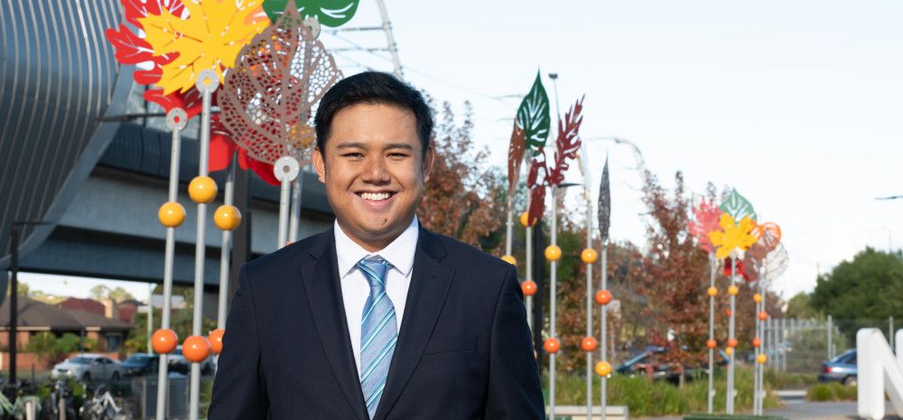 A man in a suit and tie smiles at the camera in front of colourful metal sculptures