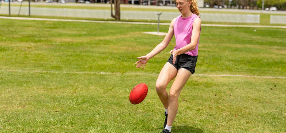 a young person kicking a football on an oval