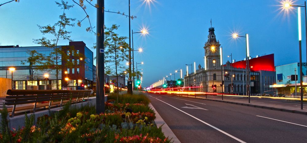 Looking down astreet at twilight with an historic clock tower and office buildings in the background