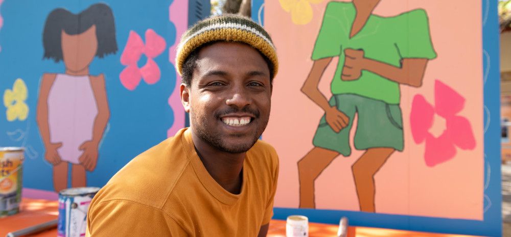 Man wearing a beanie and smiling at the camera in front of brightly painted art panels.