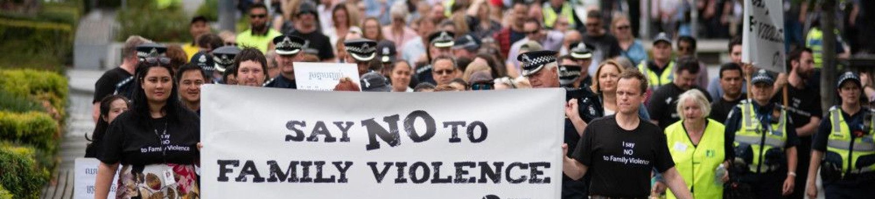 group of people marching with banner saying say no to family violence