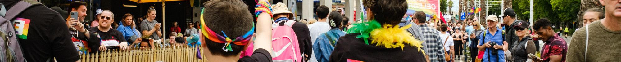 A group of people walking down a street lined by crowds under a banner that reads Greater Dandenong Pride