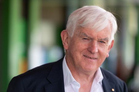 Man with white hair, dressed in a white shirt and black jacket, smiling at the camera